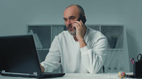 Mature Male Employee is Answer the Phone Call and Using Laptop Computer Working Alone in Office