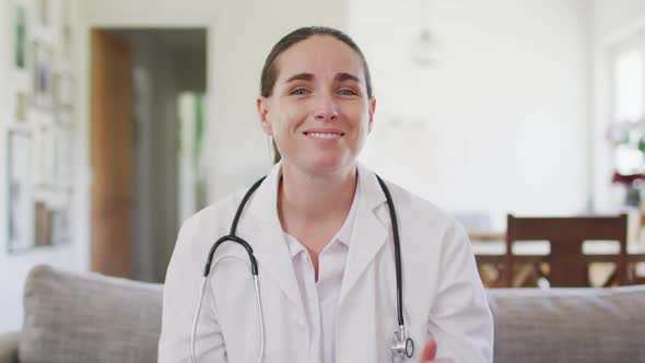 Happy caucasian female doctor sitting on sofa having video call