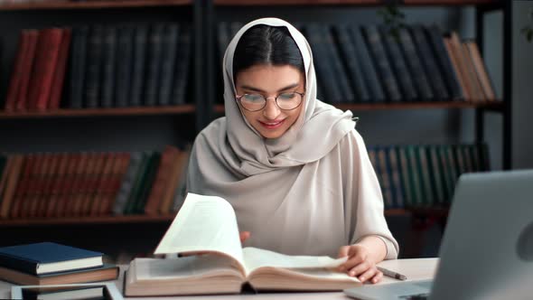 Muslim Woman in Hijab Reading Book Prepare to Exam at Public Library Desk with Laptop