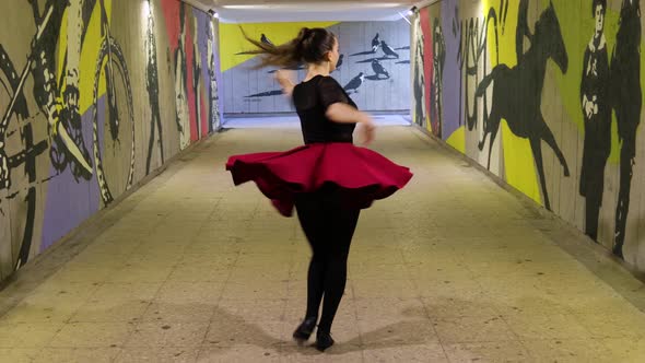 Beautiful dancer practices dancing in graffiti covered passage