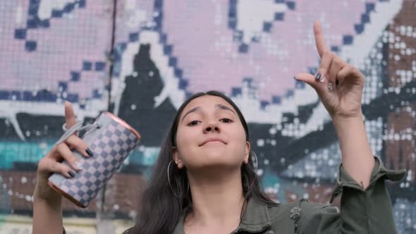 A Young Hipster Girl in a Good Mood Is Dancing To the Music While Holding in Her Hand a Portable