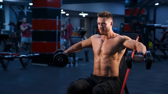 Handsome power athletic man bodybuilder doing exercises with dumbbells.