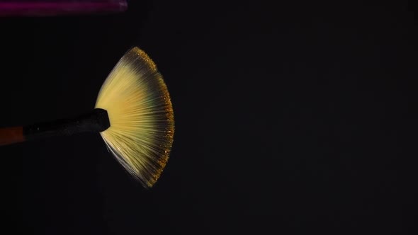 slow motion of a make up brush with gold powder explosion and burst on black background