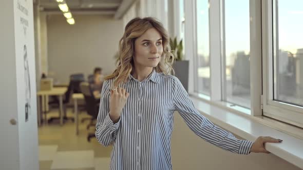 Young American Woman is Posing and Watching Window in Office Room