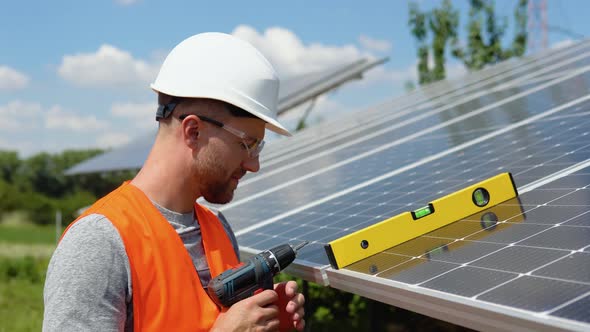 Male Engineer in Protective Helmet Installing Solar Photovoltaic Panel System Using Screwdriver