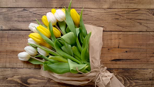 Take yellow and white tulips bouquet from a wooden table top view 