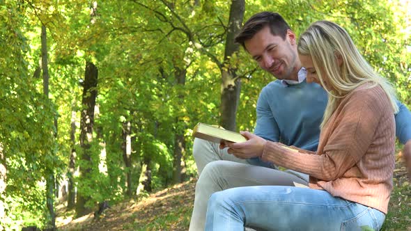 A Young Attractive Couple Sits in a Park on a Sunny Day, the Man Gives the Woman a Present