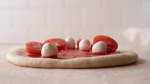 Camera follows putting tomato and mozzarella cheese on a pizza dough. Slow Motion.