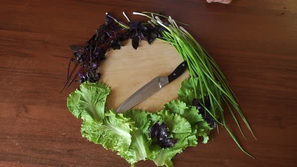 Fresh Vegetables and Herbs Lie Around a Round Cutting Board with Knife on Table