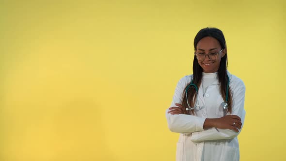 Black Female Doctor in Lab Coat Smiling To the Camera on Yellow Background.