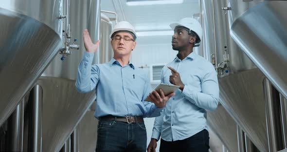 Two Industry Engineers Walk in Factory Use Tablet and Discuss Work