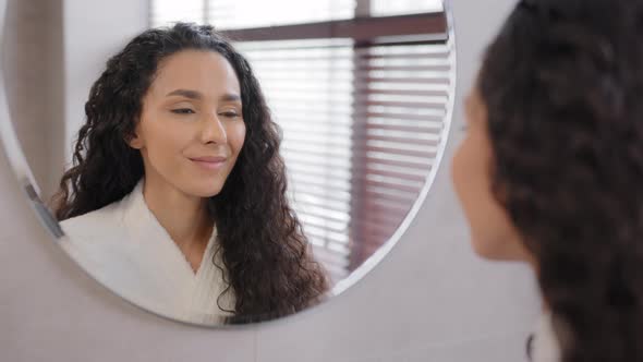 Young Calm Attractive Woman in Bathrobe Stands in Bathroom Looks in Mirror Admiring Reflection Enjoy