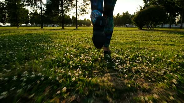 Sporty Women Legs in Tights and Sneakers Running Across the Grass at Sunset