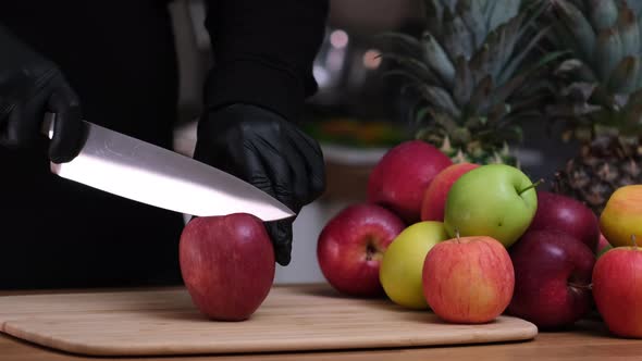 Cuts an apple in half with a knife. Human hands in black gloves cut fruits