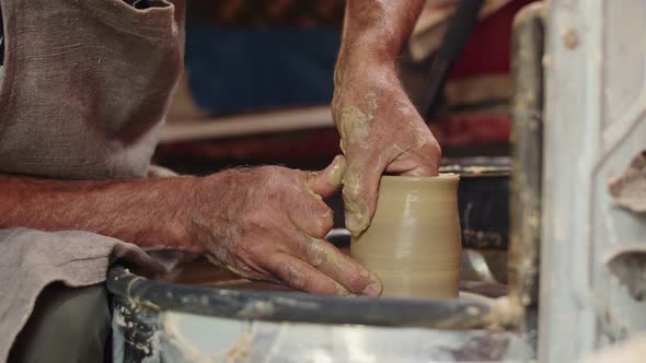 Professional potter in apron turns clay on potter's wheel and gives product thin walls.