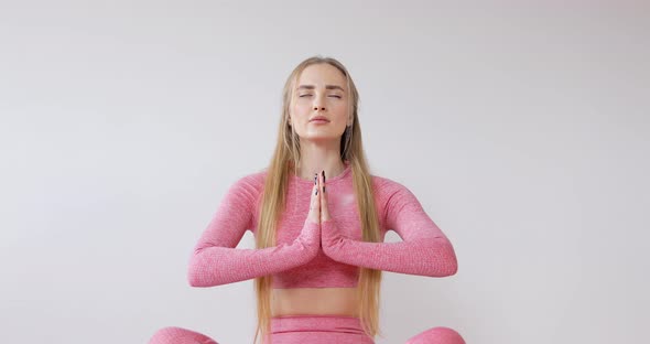  Woman in pink sportswear is meditating in lotus butterfly position sitting on a yoga