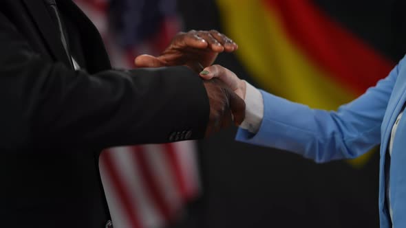 Handshake of African American Male and Caucasian Female Hand at Background of National Flags