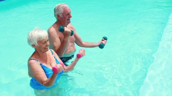 Senior couple exercising with dumbbells in the pool