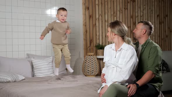 Parents Look at Toddler Son Jumping and Falling on Bed