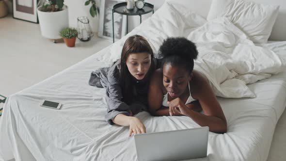 Affectionate Lesbian Couple with Laptop Lying on Bed