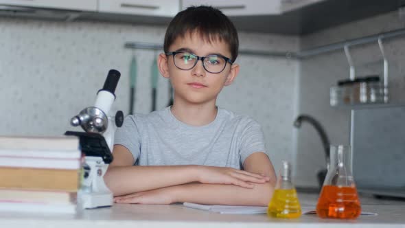 A Schoolboy Looks at the Camera and Smiles While Sitting at Home in the Kitchen Next To a Microscope