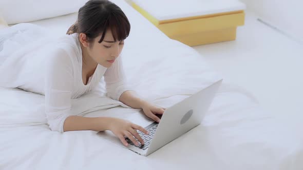 Young asian woman lying on bed using laptop computer shopping online at bedroom.