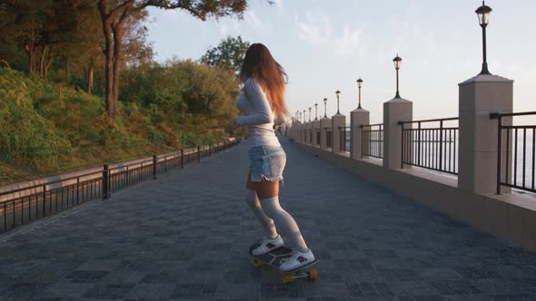 Young Stylish Attractive Woman Skateboarding at Sunrise on Seafront Slow Motion