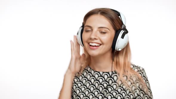 Young Beautiful Blonde Girl Smiling Listening Music in Headphones Dancing Singing Over White