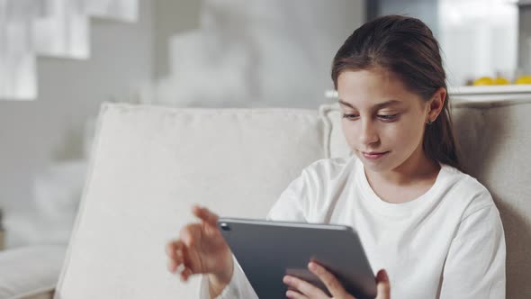 Relaxed Female Child Sitting on Sofa with Tablet in Hands