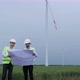 Engineers look at project sheet in hands and point to wind turbine generating electricity. - VideoHive Item for Sale