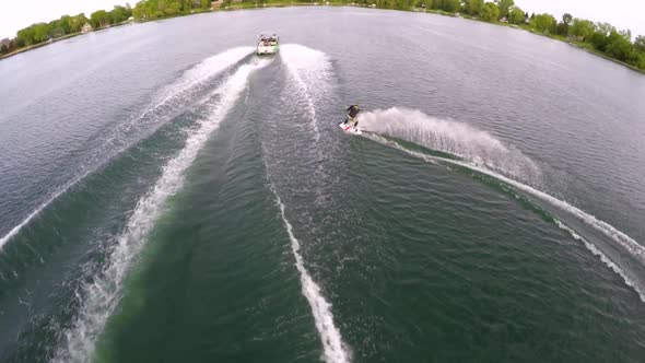 Aerial birds-eye drone view of a man wakeboarding behind a boat.