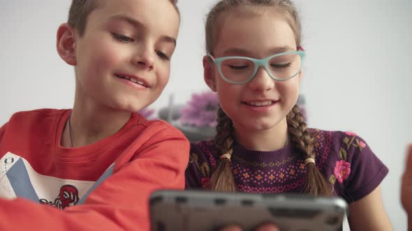 Smiling Childrens Looking at Mobile Phone. Boy and Girl Watching Cartoon at Home