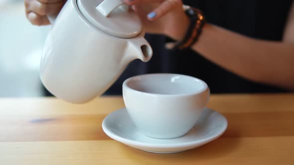 Close Up View of Female Hands Pouring Hot Tea From the Teapot in the White Porcelain Cup on the