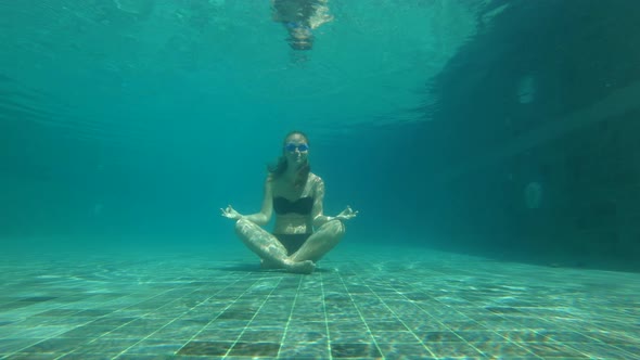 Slowmotion Underwater Shot of a Young Woman in a Yoga Pose Meditating on a Bottom of a Swimming Pool