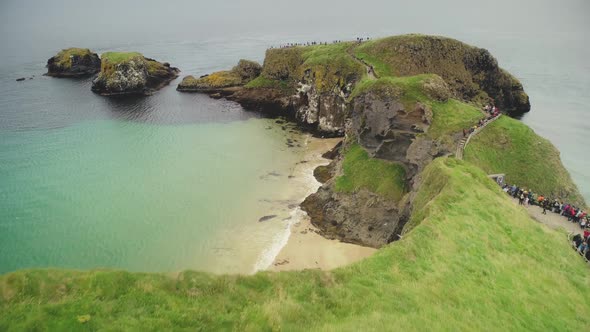 Irish Ocean Aerial View: Tourists Walk on Rope Bridge, Carrick Island, Northern Ireland