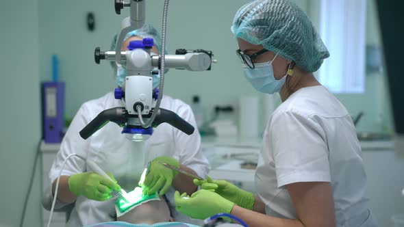 Side View Professional Dental Assistant Passing Instruments to Doctor at Dental Microscope in Slow