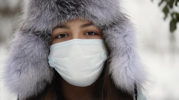 Portrait of a Teen Girl Wearing Protective Face Mask and a Fur Winter Hat Outdoors