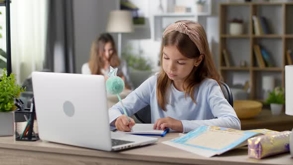 Girl Writes in a Notebook on an Online Lesson at Home in the Living Room