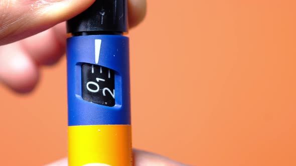 Close Up of Hand Holding Orange Color Insulin Pens on Color Background 