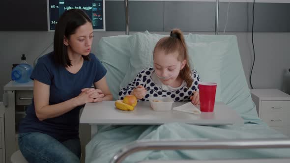 Mother Sitting with Sick Child Patient While Eating Healthy Food Lunch in Hospital Ward