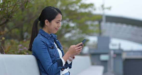 Woman Look at Mobile Phone and Sit on The Outdoor Bench