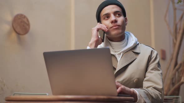 Positive Arabian man working on laptop and talking by phone