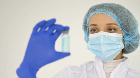 A Female Doctor in a Face Mask and in Medical Blue Gloves Shows a Ampoule with Coronavirus Vaccine