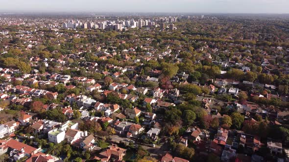 Aerial flyover rural residential area in Buenos Aires with green trees and block complex in backgrou