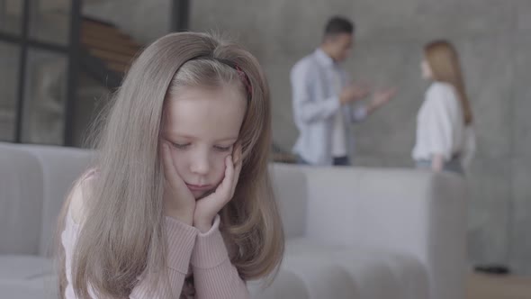 Little Sad Girl Sitting on the Sofa in the Foreground with Her Head on Hands While African Ameican