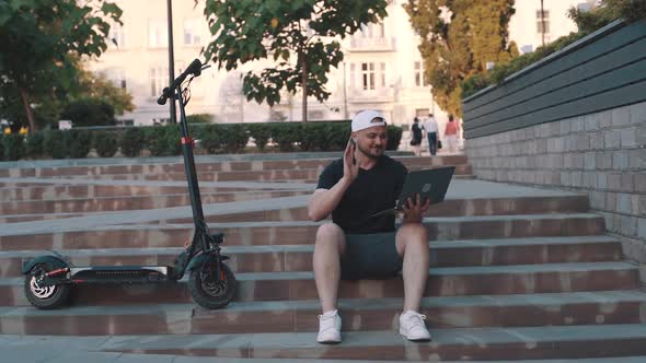 Adult Man Well Dressed with Electric Scooter Working with His Laptop in the Street in the City