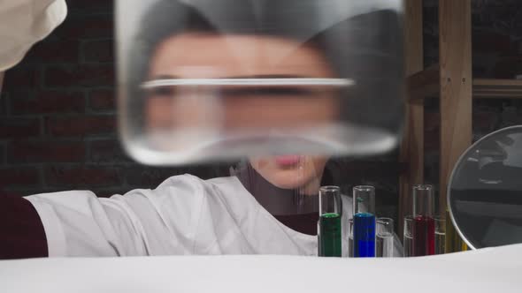 Lab Assistant with Face Shield of Puts Beaker Onto Table