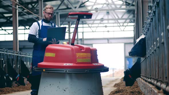 Livestock Farmer is Operating a Robot By His Laptop