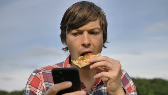 Man Surfs Internet with Phone Eating Pizza in Green Park