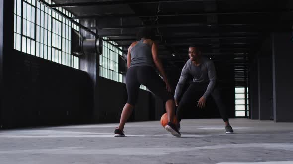 African american man and woman standing in an empty building playing basketball